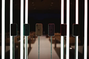 Several smartphones are displayed on stands, illuminated by vertical, glowing light bars. The setting appears to be a modern, dimly lit environment possibly in a retail or exhibition space.