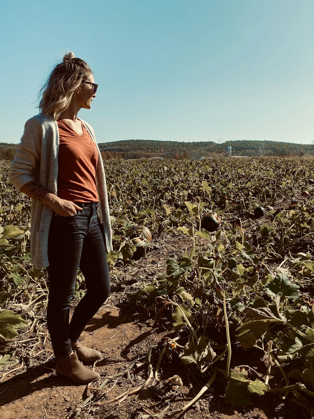 woman wearing orange shirt and cardigan standing near green plants during daytime