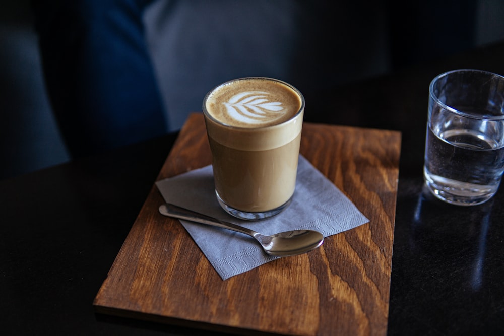 cappuccino dans un verre à boire près d’une cuillère en acier inoxydable gris