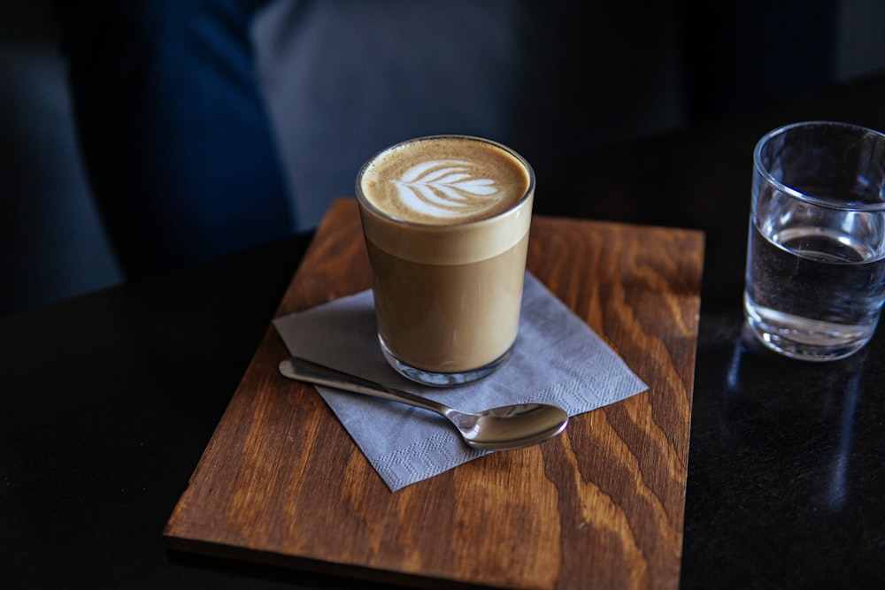 cappuccino in drinking glass near gray stainless steel spoon