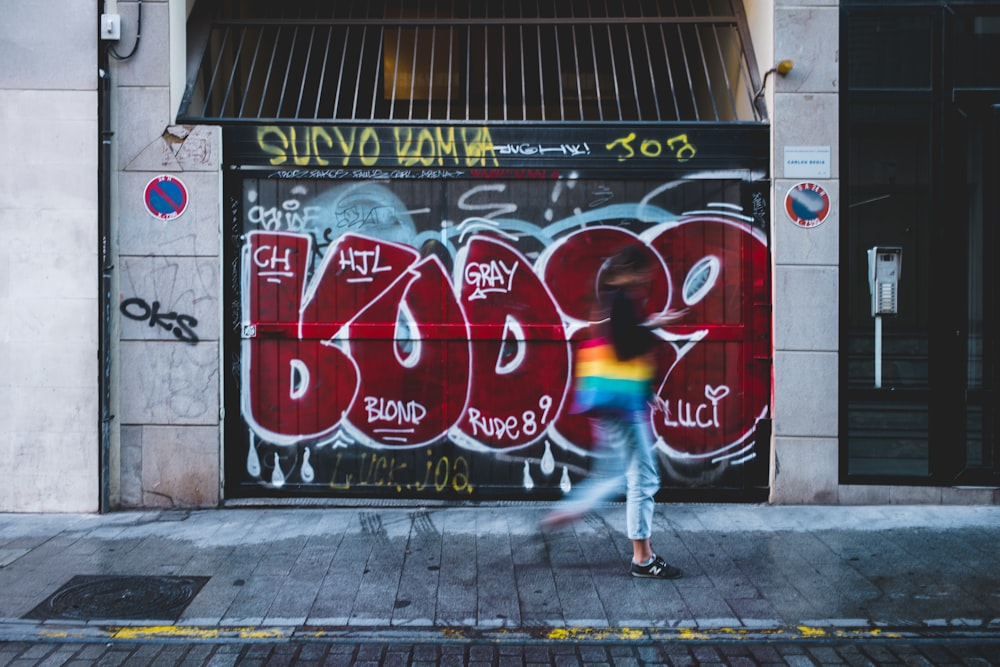 woman walking on sidewalk beside graffiti wall