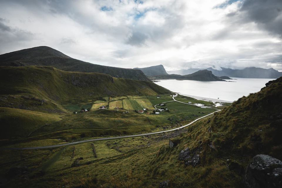 Serene landscape with small village at foot of mountain range under overcast sky