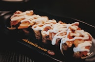 A plate with pieces of sushi topped with a generous amount of white sauce, on a dark serving dish with a restaurant logo partially visible.