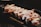 A plate with pieces of sushi topped with a generous amount of white sauce, on a dark serving dish with a restaurant logo partially visible.
