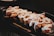 A plate with pieces of sushi topped with a generous amount of white sauce, on a dark serving dish with a restaurant logo partially visible.