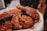 Crispy, golden-brown fried chicken pieces are covered with a glossy, slightly sticky sauce, sprinkled with sesame seeds, and placed on a paper-lined tray.