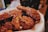 Crispy, golden-brown fried chicken pieces are covered with a glossy, slightly sticky sauce, sprinkled with sesame seeds, and placed on a paper-lined tray.