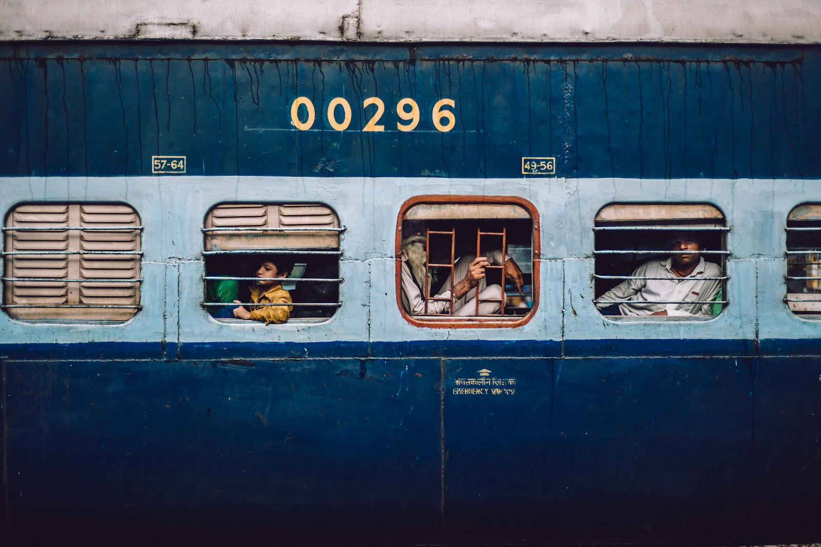 A blue Indian Railways coach with passengers at the windows