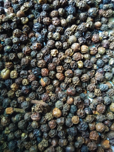 Close-up of freshly harvested black peppercorns and cardamom pods on a rustic wooden table.