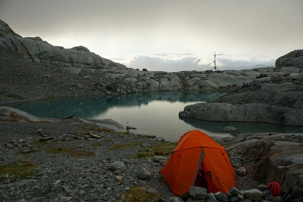 orange tent beside calm body of water