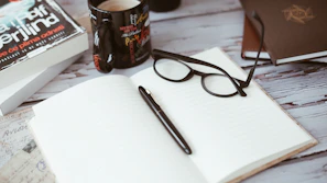 An inviting café table strewn with an open book, reading glasses, and a notebook.