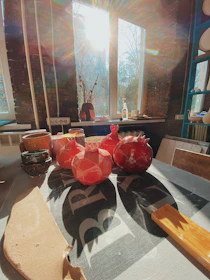 A sunny windowsill displaying an assortment of hand-thrown plates and cups glowing softly in natural light.