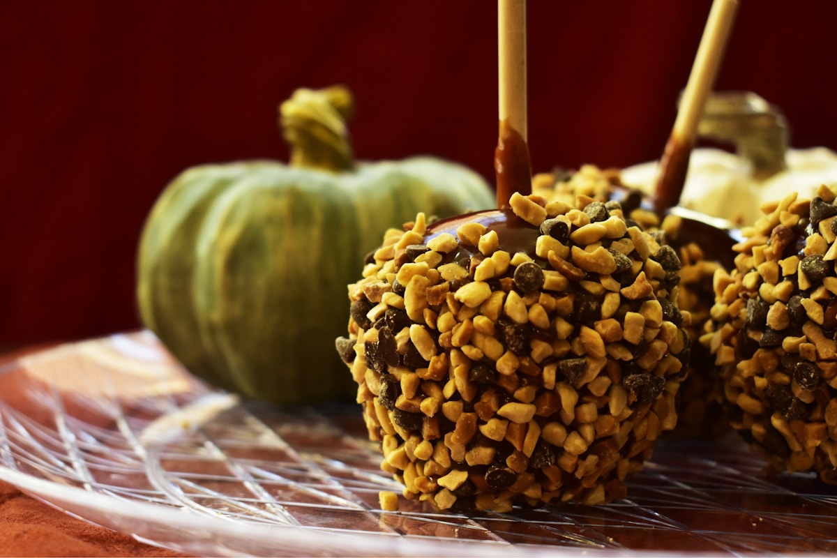 Caramel apples on wooden sticks rolled in chopped nuts, beside a small green pumpkin