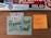 A wooden surface displays several colorful stickers and notes. At the top, there are various tech and brand stickers like 'bitly', 'vimeo', and 'code'. Below them, two notes are stuck to the surface: one is a light green card with the phrase 'Try Organic Food' accompanied by a vintage illustration of a basket of vegetables; another is a bright orange sticky note with the handwritten message 'FOR JUNO :)'. Additionally, there's a sticker with 'USERS FIRST' written in multicolored letters.