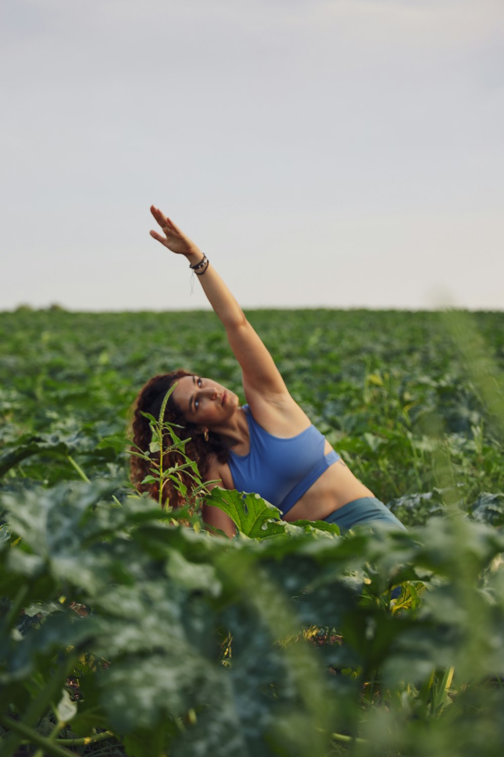 selective focus photography of woman raising her left hand while sitting on ground surrounded by plants