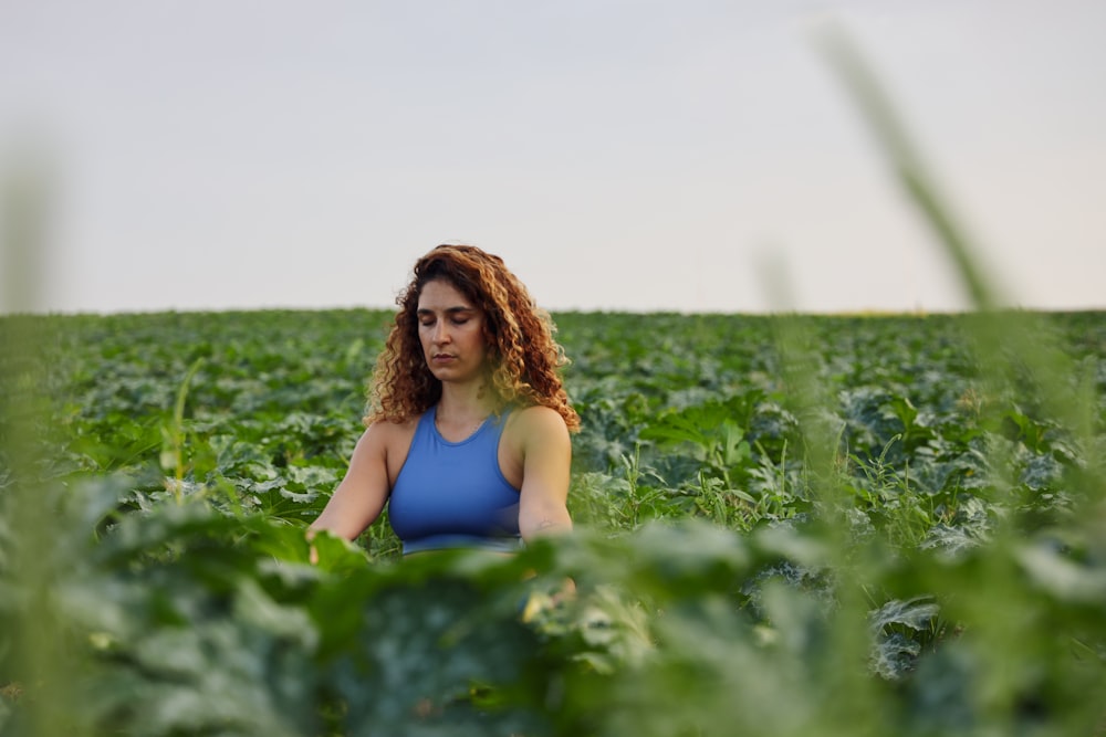 selective focus photography of woman meditating while sitting on ground surrounded by plants during daytime