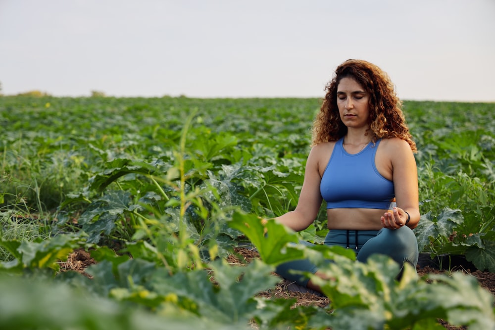 woman in blue sports brassiere meditating on plant field