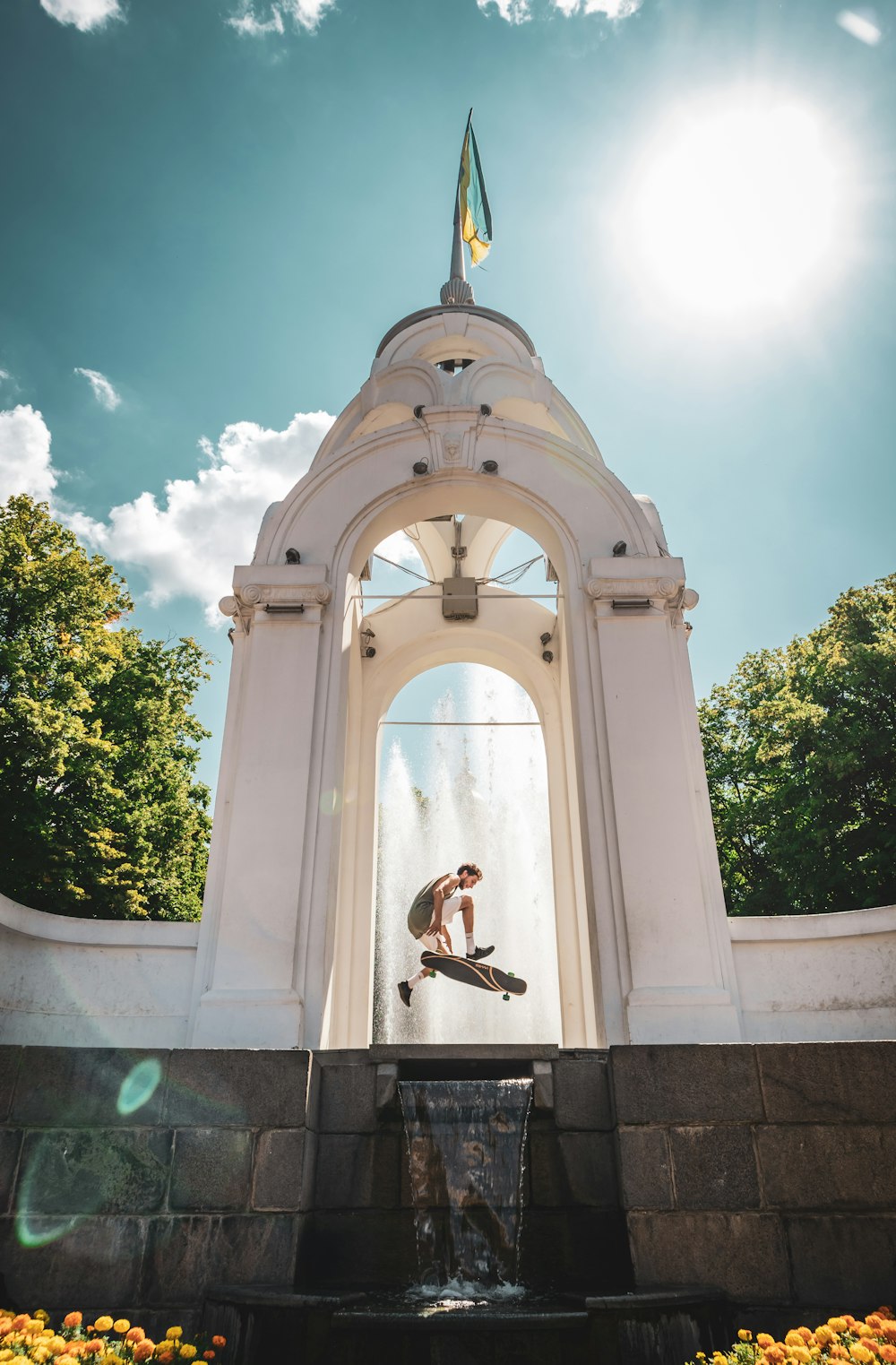 man doing longboard tricks under the arch near fountain