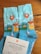 A pair of blue socks with colorful patterns including mountains, trees, a sailboat, and a red map marker. Beside the socks is a card with text expressing gratitude and encouragement, adorned with small illustrated icons.