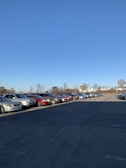 Spacious parking area surrounded by tall trees under a clear blue sky.