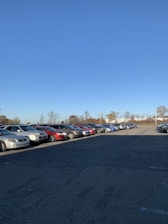 A spacious parking lot under a clear blue sky with parked vehicles in neat rows.