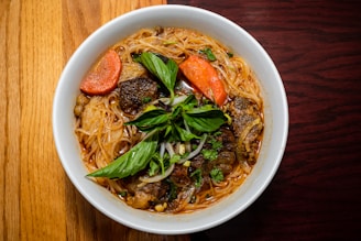 A vibrant bowl of konjac noodles topped with fresh vegetables and herbs on a rustic wooden table.