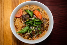 Freshly cooked noodles garnished with herbs, served in a traditional bowl on a wooden table.