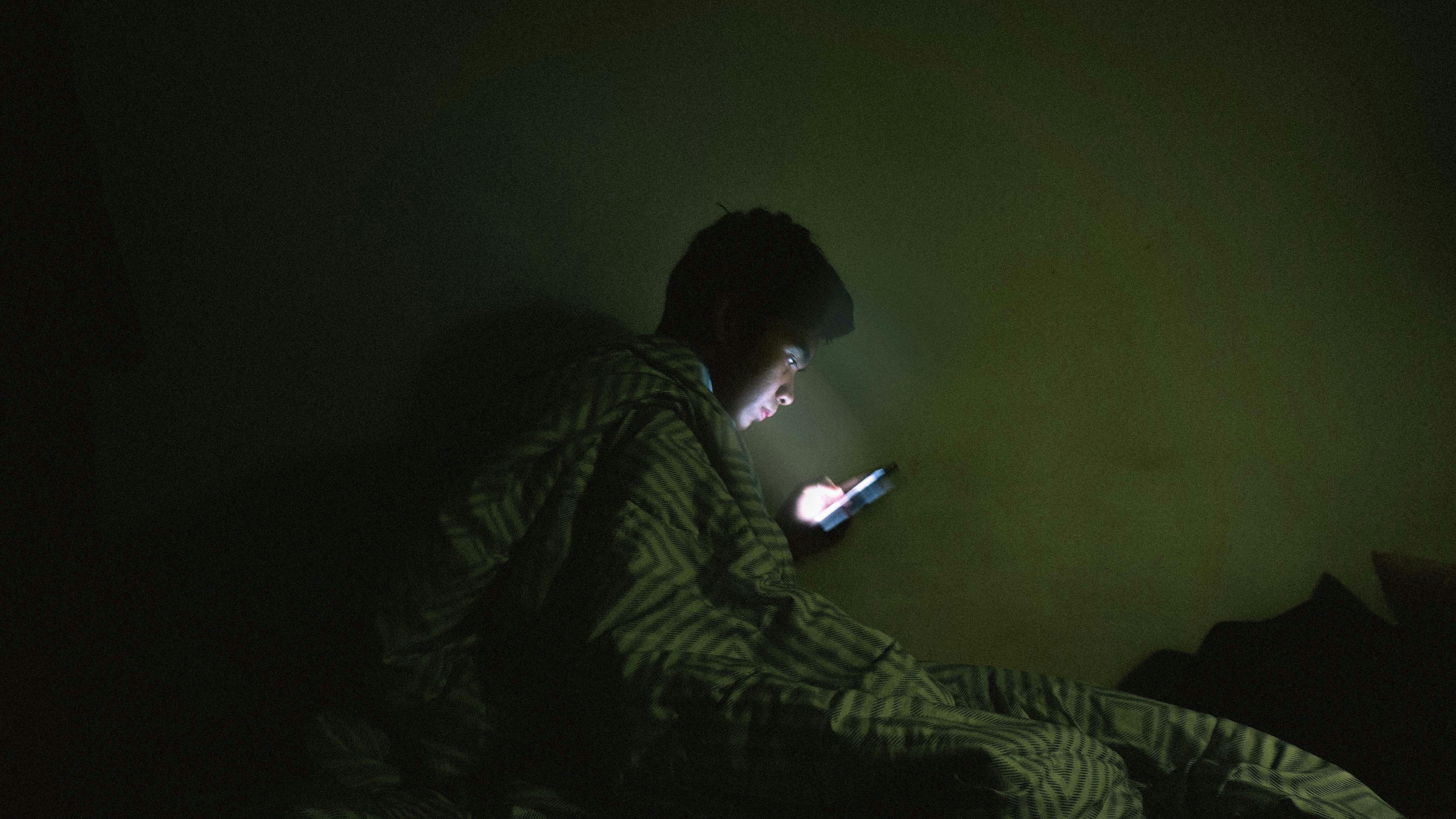 Person illuminated by smartphone screen in dark room