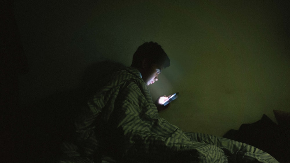 man using mobile phone while covering his body of blanket