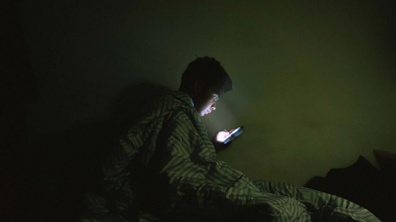 A person wrapped in a blanket, lit only by a phone screen