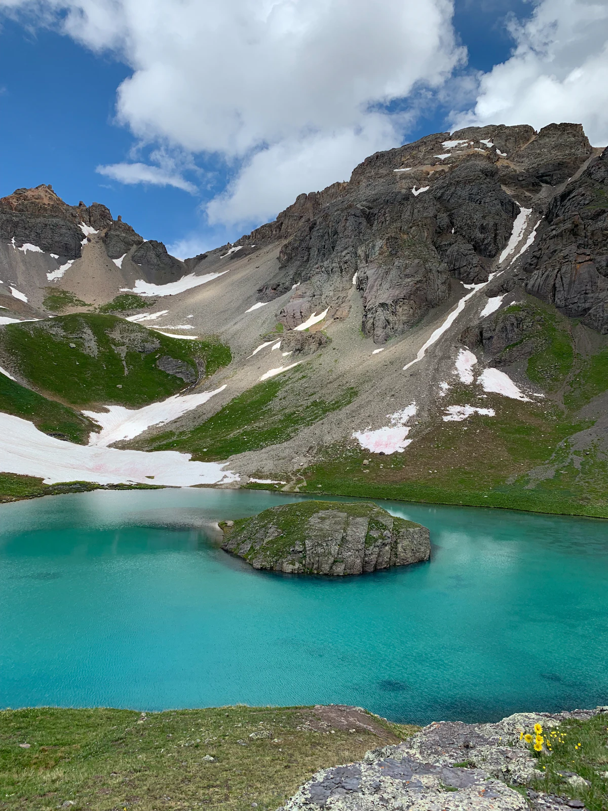 A turquoise lake with a small rocky island in Ice Lake Basin, below snowy cliffs