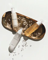 Close-up of luxurious beauty products arranged on a golden tray reflecting the brand colors.