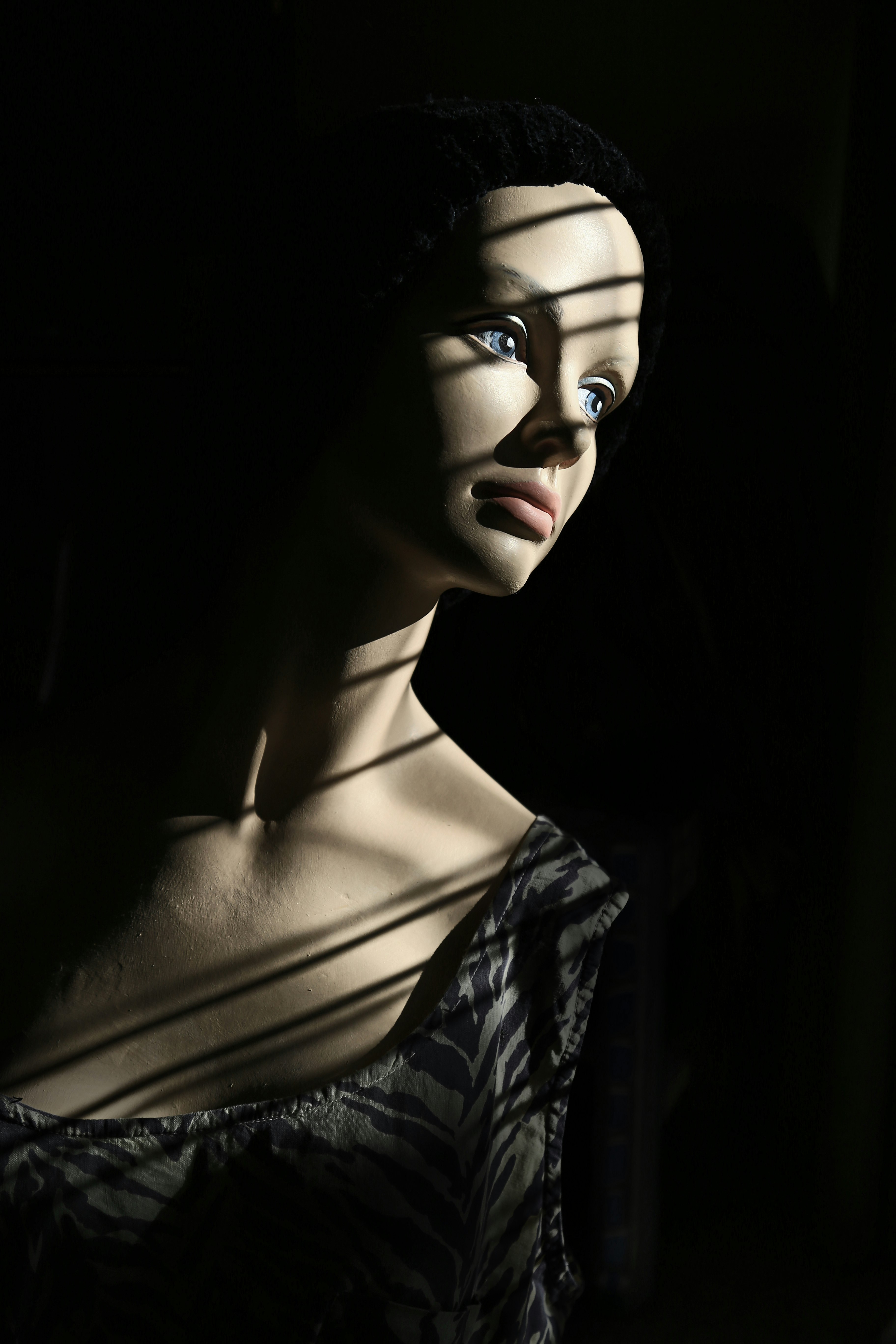 Beautiful mannequin with no arms sits in dramatic sun and shadow.