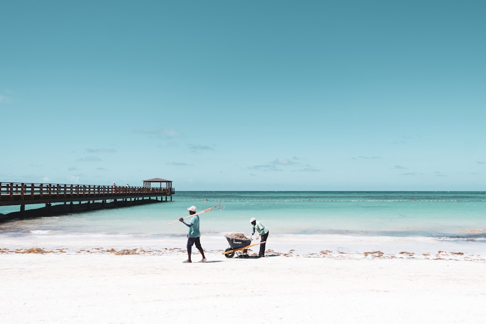 Dos personas empujando una carretilla en la orilla del mar