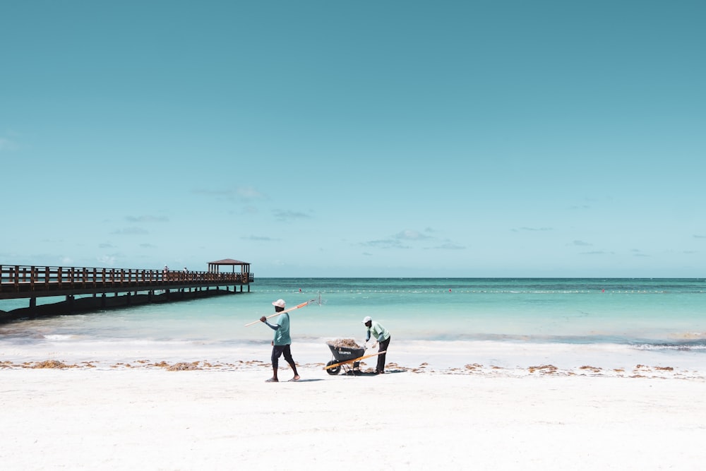 two people pushing wheelbarrow on seashore