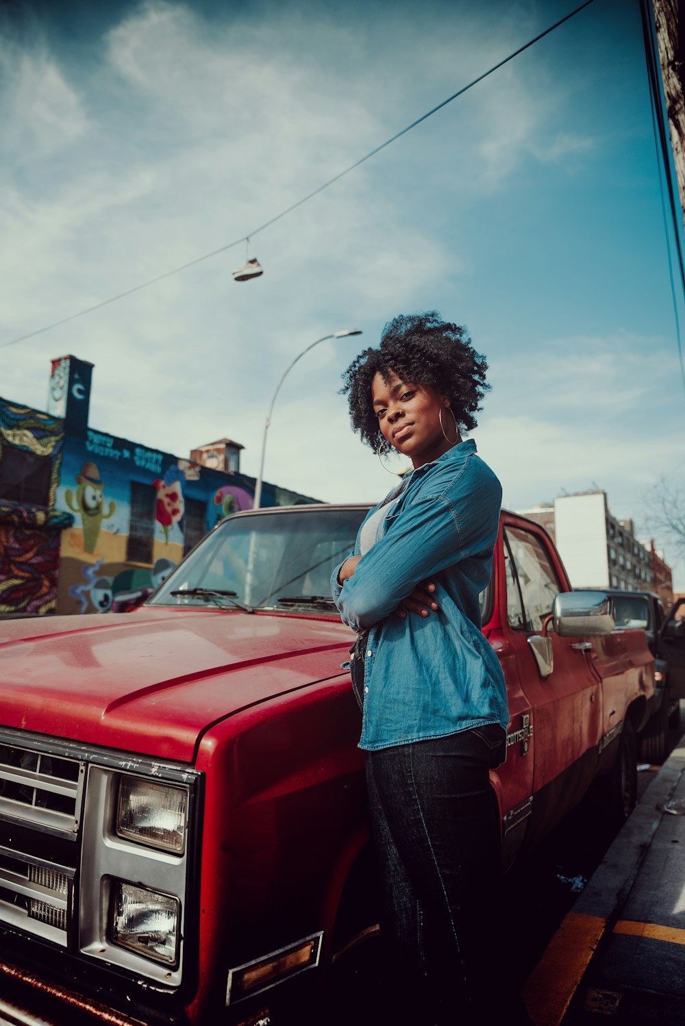 woman in blue jacket standing beside red pickup truck during daytime