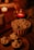 A cozy and warm scene featuring a striped popcorn bucket topped with a plastic spider, surrounded by candles and blankets. Three ghost-themed cupcakes are placed on a wooden platter, enhancing the Halloween theme.