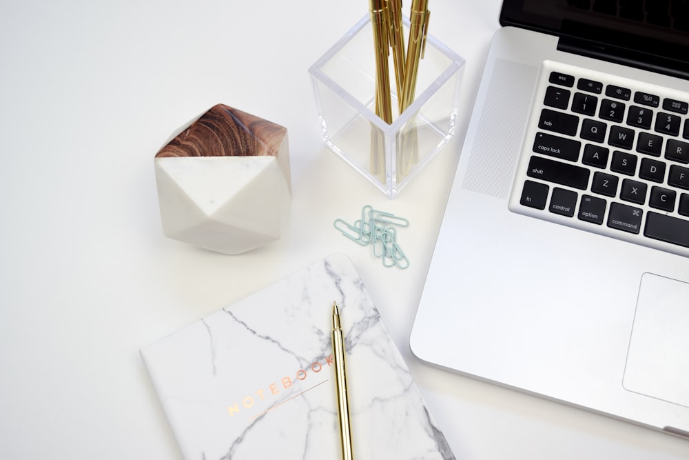 gold pen on white book beside MacBook Pro