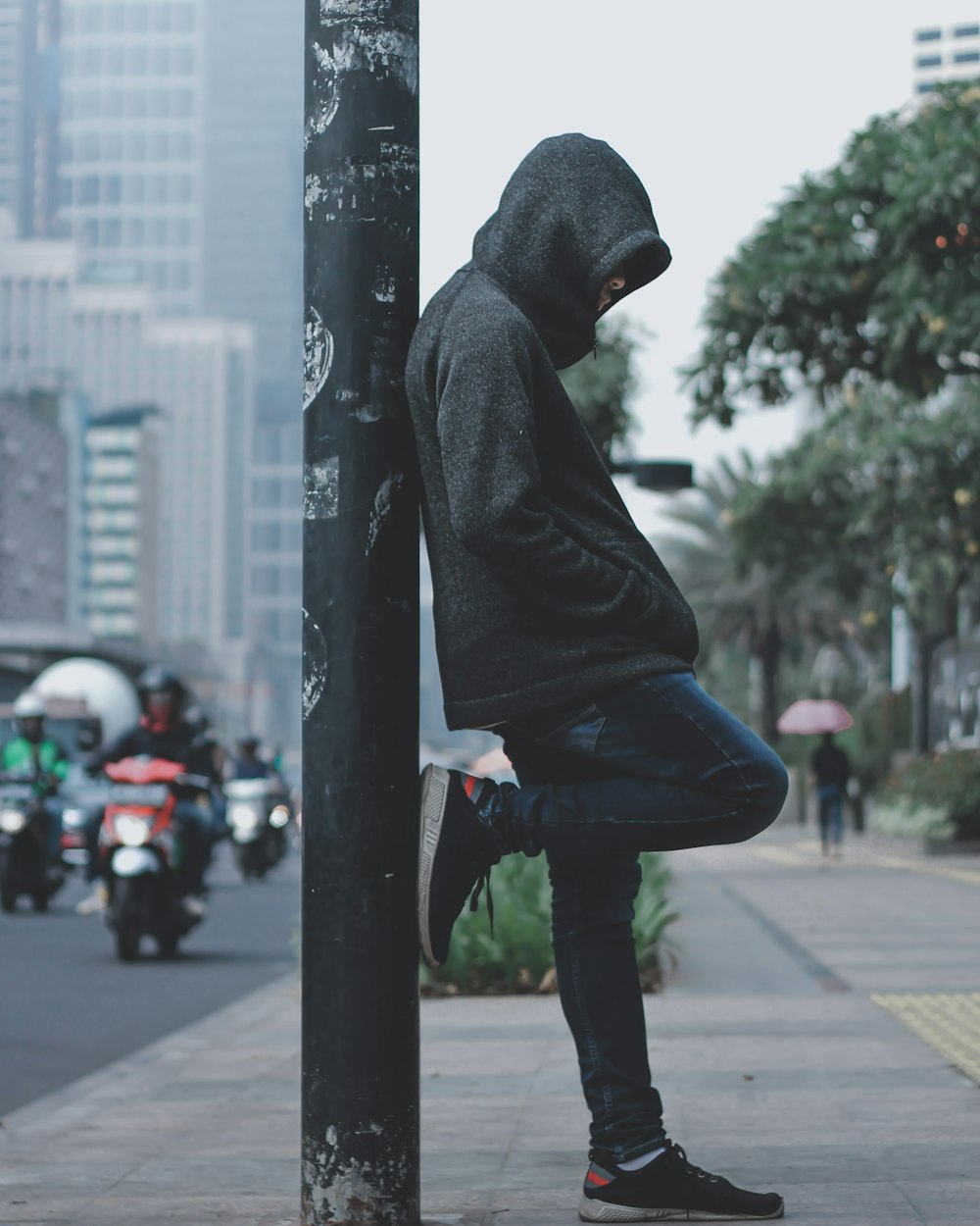 person in gray hoodie leaning on post