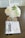 A vase with white flowers and green leaves is placed on a table. Nearby is an open book titled 'Imitation of Mary' along with a pearl rosary adorned with a cross. The setting is calm and serene, with soft lighting enhancing the peaceful atmosphere.