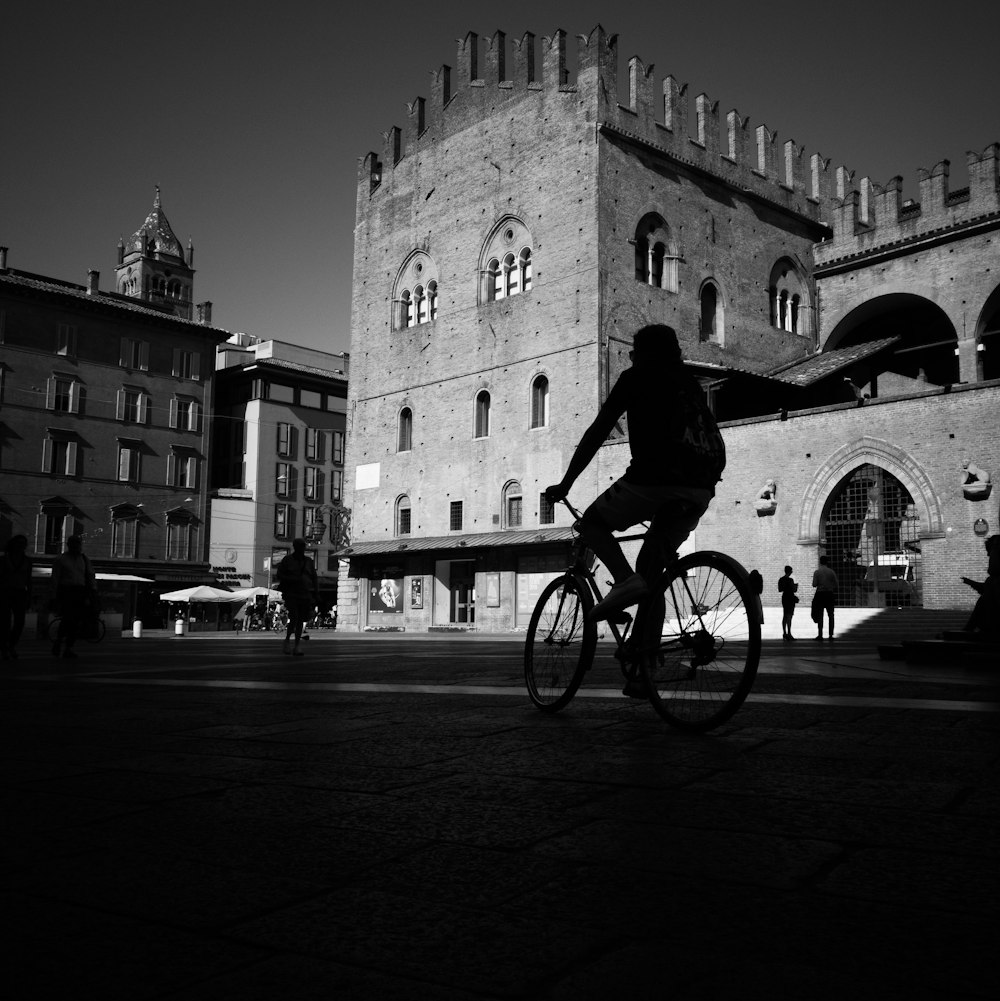 grayscale photo of man biking in front of castle