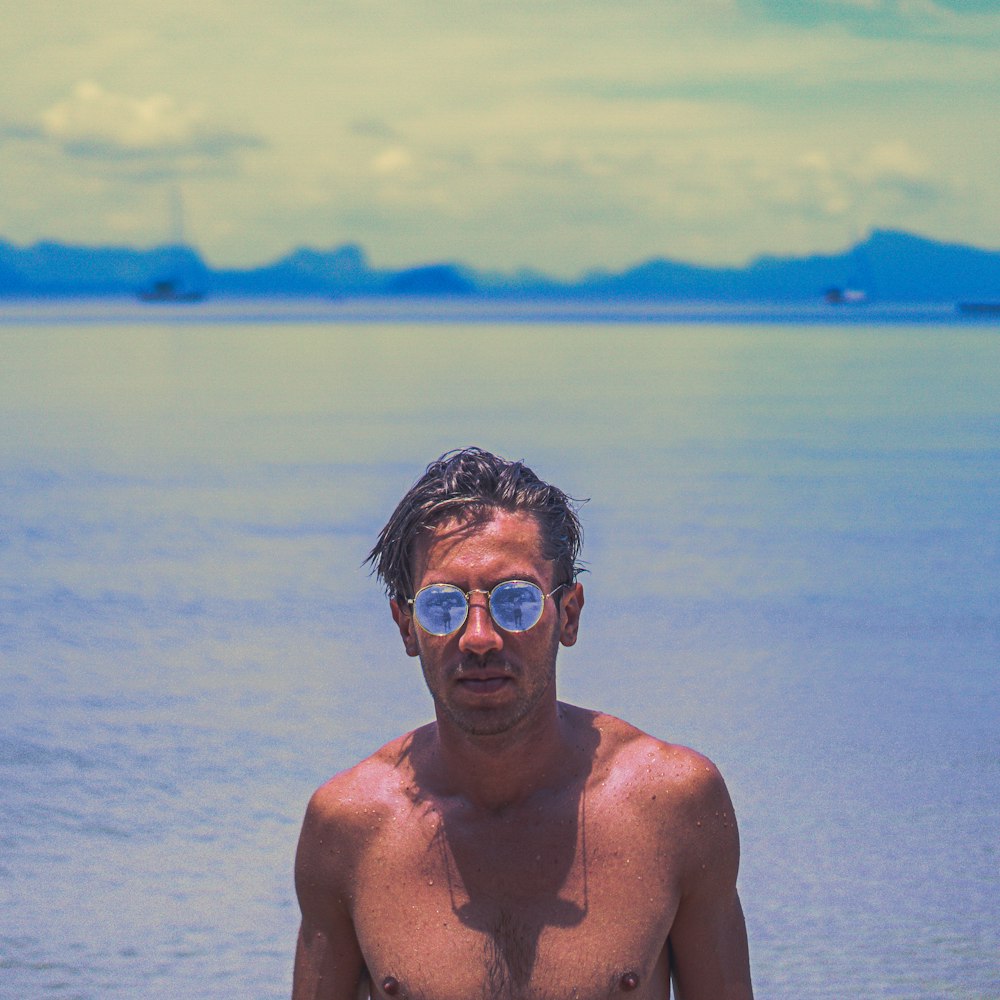 uomo in occhiali da sole color oro dietro il mare