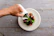Bright kitchen scene showing a smiling woman spraying Verde Vitale cr videy spray onto a salad.