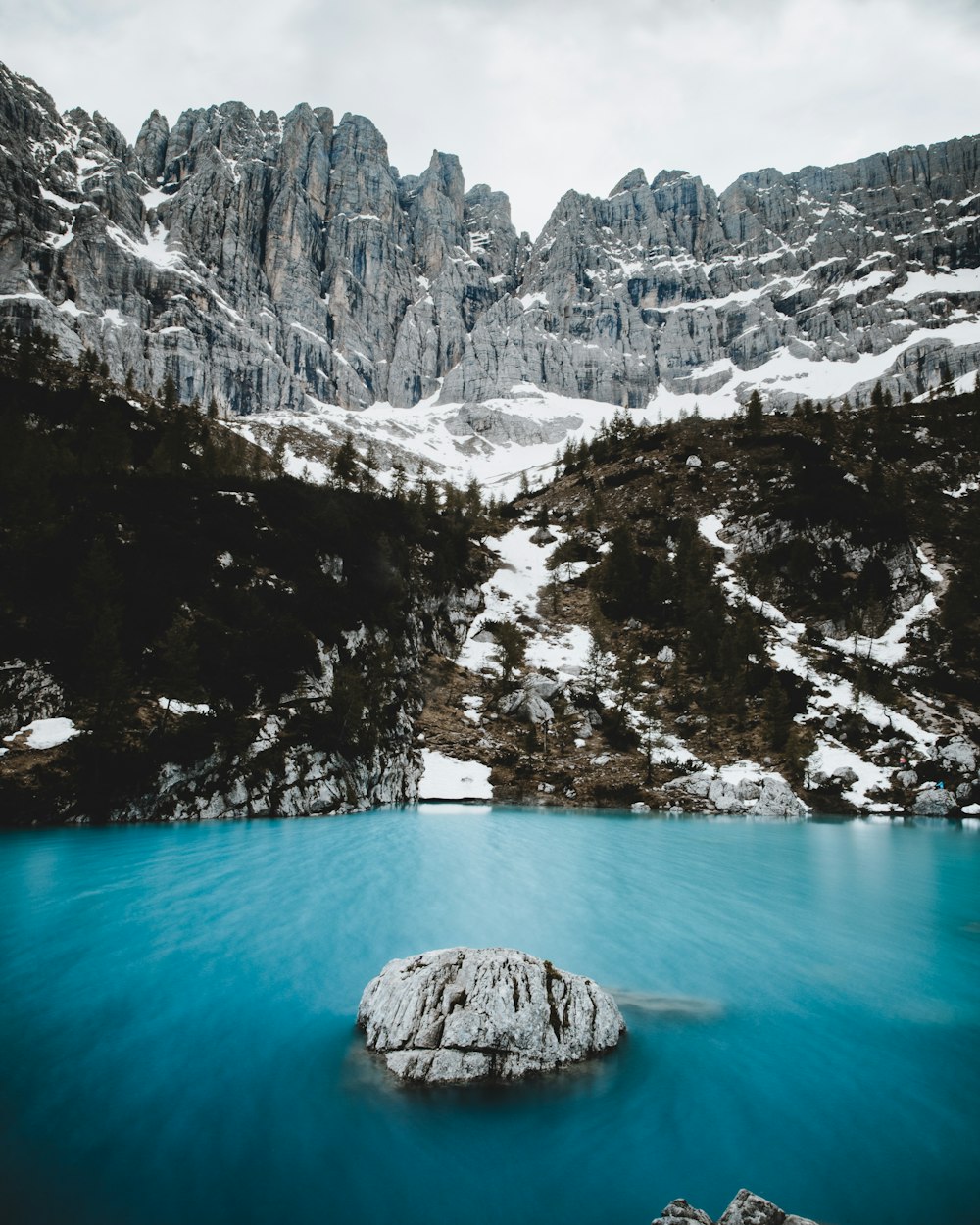 blue water near rock mountain with pine trees