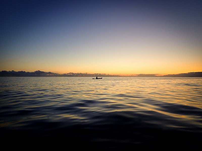Sailing boat silhouetted on calm water at sunset