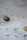 A close-up view of a fabric with a delicate embroidery pattern featuring oval cutouts and stitching on a soft, white background. Two buttons with a sheen, one black and one gold, are sewn onto the fabric, adding subtle contrast.