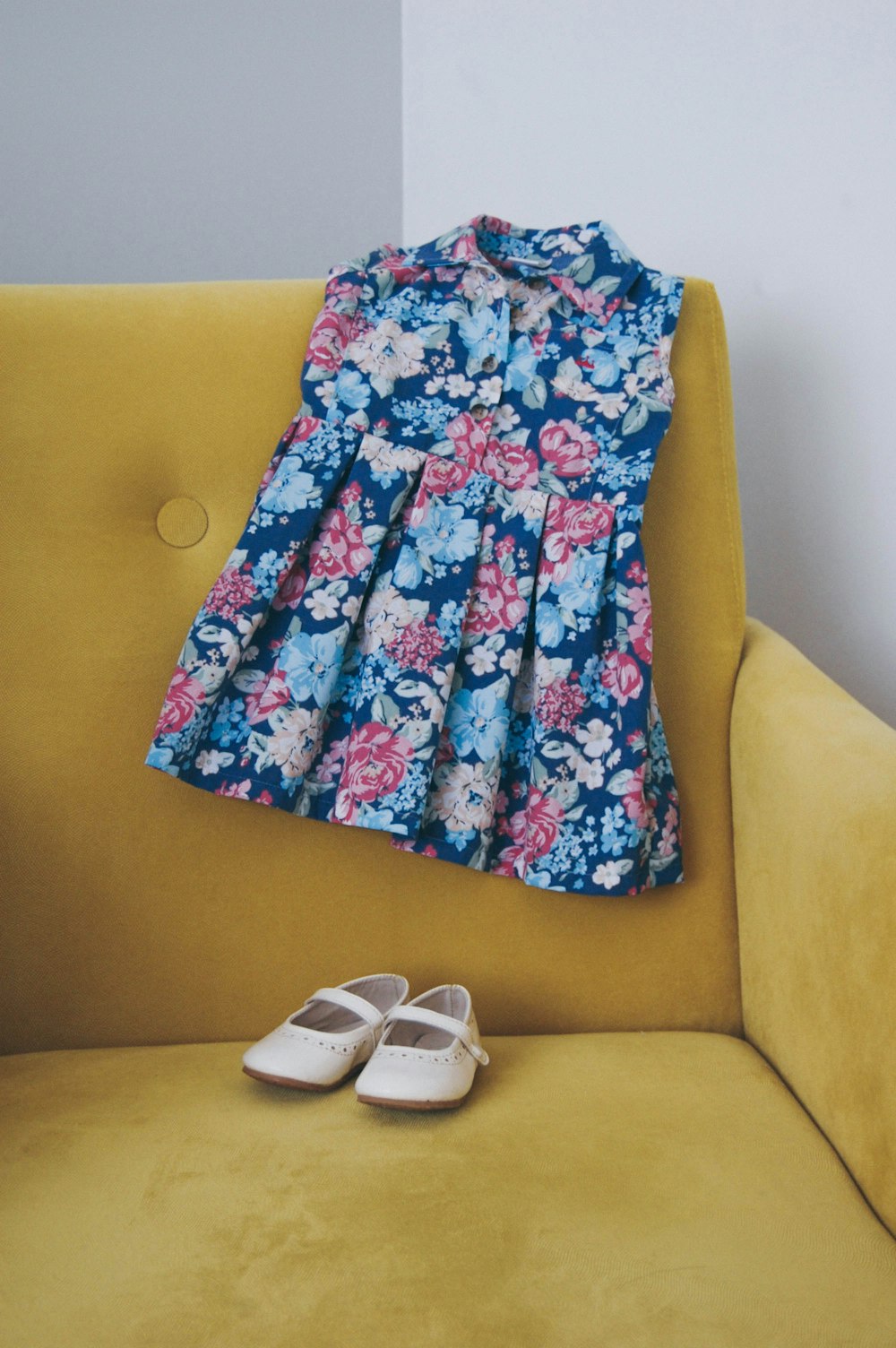 vestido floral azul e multicolorido e sapatos de couro branco no sofá