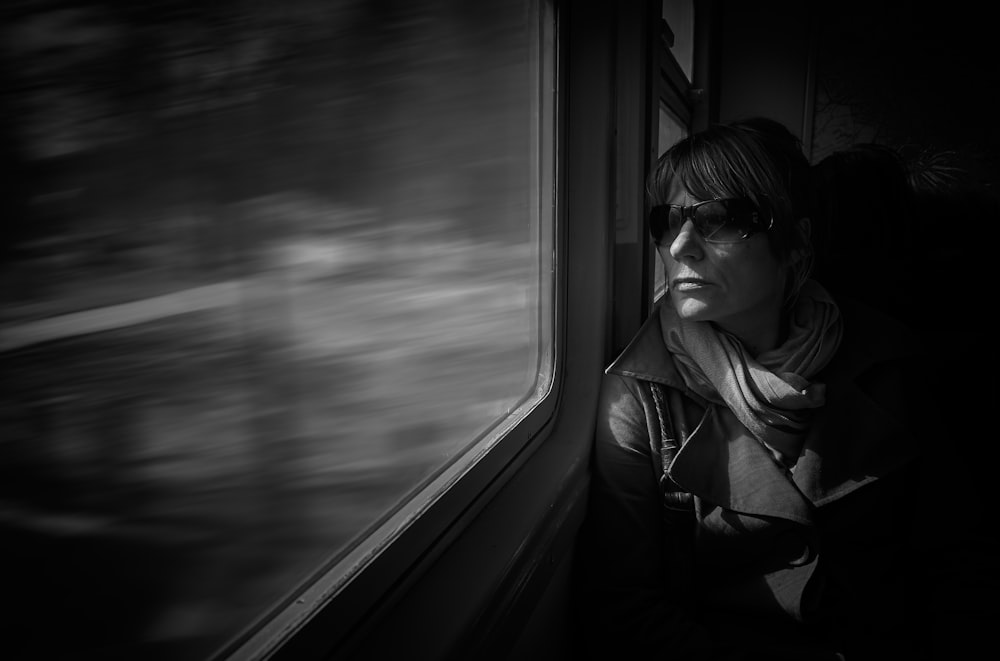 a black and white photo of a woman looking out a window