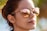 A person wearing reflective sunglasses that show a beach scene with palm trees and a structure in the reflection. The background is slightly blurred, emphasizing the focus on the reflective surface of the sunglasses.