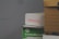 A stack of cardboard boxes, with the top box labeled 'FRAGILE' in red text. Below it, a green box marked 'Sustainable Earth' is visible. Another box, brown with black stripes, is partially in view on the right.